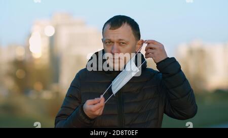 Uomo in piedi sulla strada mettendo su un medico monouso maschera Foto Stock