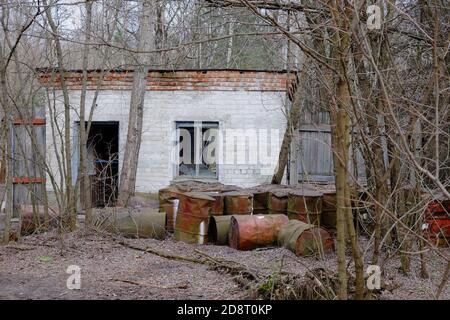 Barili di metallo arrugginiti vicino ad un edificio abbandonato di mattoni. Edificio nella zona di esclusione di Chernobyl. Foto Stock