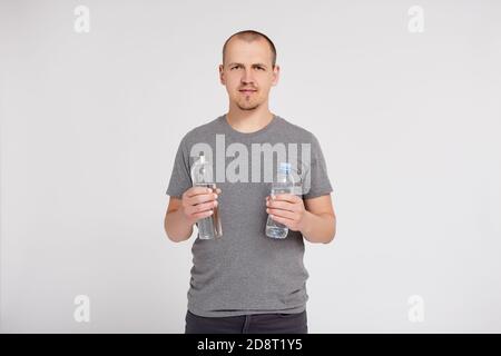 zero sprechi e concetto eco-friendly - giovane uomo a confronto flacone in vetro riutilizzabile con bottiglia d'acqua in plastica su grigio sfondo con spazio di copia Foto Stock