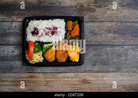 Scatola bento giapponese colorata 'Sake-katsu' con torta di pesce al salmone, riso, insalata di noodle e verdure. Rustico di legno scuro sfondo tavolo. Foto Stock