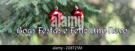 Saluti di festa in portoghese, Brasile significa Felice Anno Nuovo. Lo sfondo sfocato dell'albero di Natale è decorato con giocattoli luminosi. Bokeh. Foto Stock