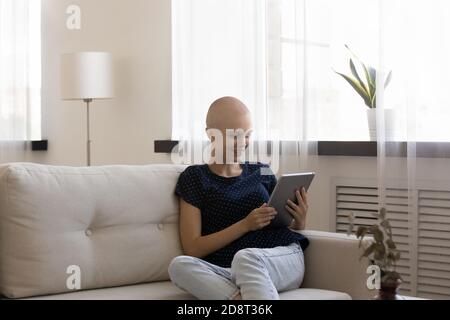 Felice donna senza capelli che tiene il tablet del computer, seduto sul divano Foto Stock