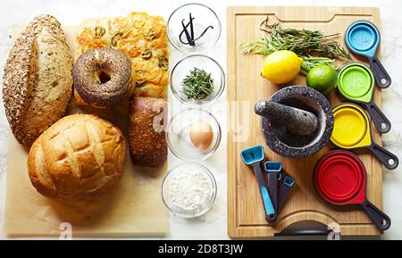 Gruppo di prodotti da forno su carta da forno con ingredienti in piccoli recipienti di vetro, dosatori e tagliere. Foto Stock