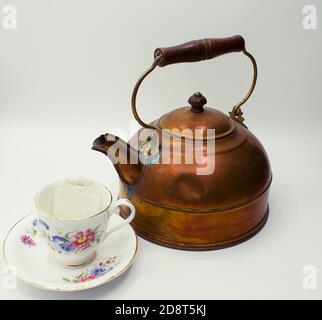 Primo piano sul vecchio bollitore di tè di rame accanto alla tazza di tè a tema floreale e il piattino. Foto Stock