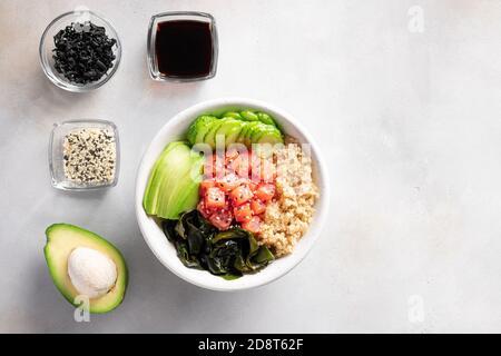 Ciotola di poke servita con salmone, avocado, cetriolo, quinoa, alghe wakame su sfondo grigio con ingredienti Foto Stock