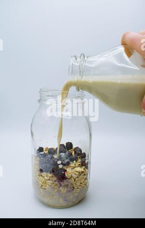 Vasetto con colazione di avena e mirtilli e latte d'avena versato in un vaso di vetro di mason. Foto Stock