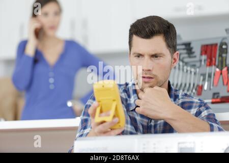 addetto alla manutenzione che utilizza un multimetro per valutare l'apparecchio da cucina Foto Stock