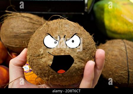 Tenere a mano il cocco con gli occhi e la bocca del cartone animato Foto Stock