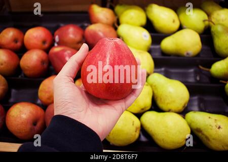 Pera rossa tenuta in mano con file di frutta in mostra come uno sfondo sfocato Foto Stock