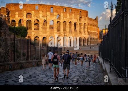 Gruppo di persone in via Sacra che cammina verso il Colosseo al tramonto nella città di Roma, Italia, l'antico anfiteatro flaviano e gli stadi dei Gladiatori Foto Stock