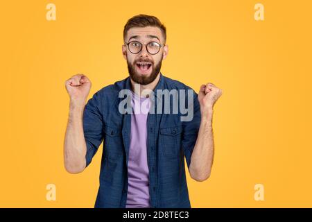 Vincitore e concetto di successo. Eccitato giovane ragazzo facendo sì gesto con pugni clenched su sfondo studio arancione Foto Stock