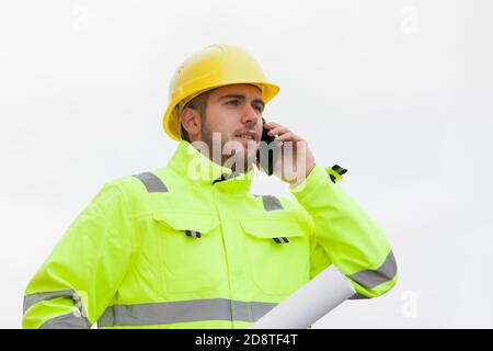 Giovane ingegnere o lavoratore con un lavoro di protezione verde indossare parlare sul telefono cellulare di fronte al cielo luminoso Foto Stock