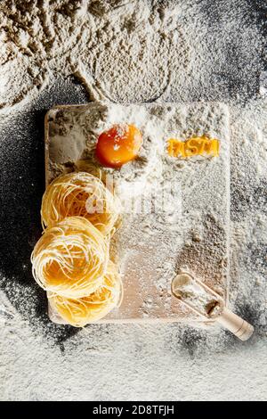 La pasta appena cotta si trova su una superficie scura spolverata con farina. Pasta italiana. Tagliatelle. Pasta cruda. Ricetta di pasta italiana. Vista dall'alto, spazio di copia Foto Stock