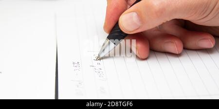 Lo studente risolve le formule matematiche. L'uomo scrive con una penna in un notebook. Compiti. Note in un notebook. Foto Stock