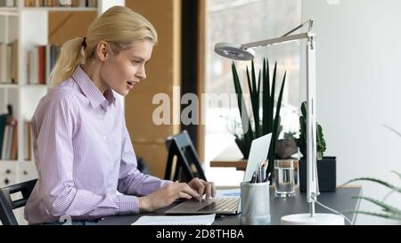 Giovane donna d'affari eccitata bionda che guarda lo schermo del calcolatore. Foto Stock