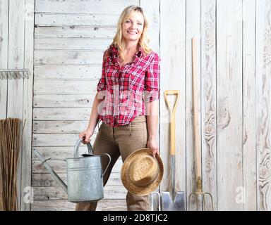 donna in orto con annaffiatura lattina su legno bianco shed sfondo con attrezzi di giardinaggio Foto Stock