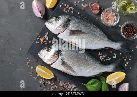 Pesce fresco pronto a cucinare dorado crudo con ingredienti e condimenti come basilico, limone, sale, pepe, cipolla rossa e olio d'oliva, vista dall'alto Foto Stock