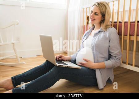 Attraente giovane donna incinta con computer portatile Foto Stock