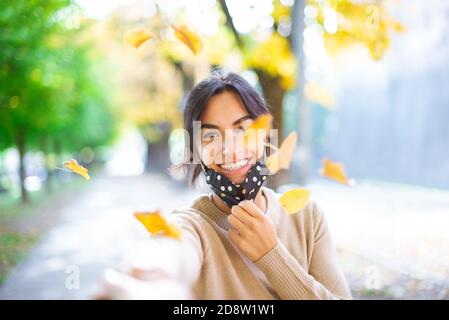 Primo piano ritratto di una bella bruna ragazza indossare protettivo Maschera viso in piedi vicino colorful autunno leaves.Art lavoro di romantico woman.new normale Foto Stock