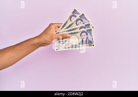 Mano ispanica che tiene 5000 yen giapponesi su sfondo rosa isolato. Foto Stock