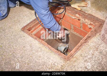 Idraulico che fissa un ancoraggio di un tubo dell'acqua in a. tombino di una casa Foto Stock