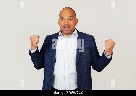 Ritratto di un giovane uomo d'affari afro-americano di successo, molto felice ed eccitato, facendo un gesto vincitore con le mani sollevate, sorridendo e gridando successo. Concetto di celebrazione. Sfondo grigio Foto Stock