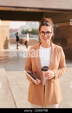 Giovane donna d'affari sorridente in occhiali e foralwear con un bicchiere di caffè Foto Stock