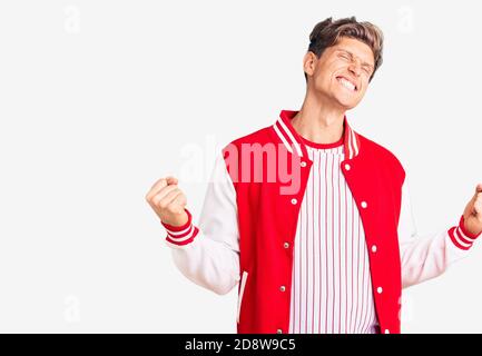 Giovane bell'uomo che indossa uniforme da baseball molto felice ed eccitato facendo gesto vincitore con braccia sollevate, sorridenti e gridando per il successo. Celebrati Foto Stock