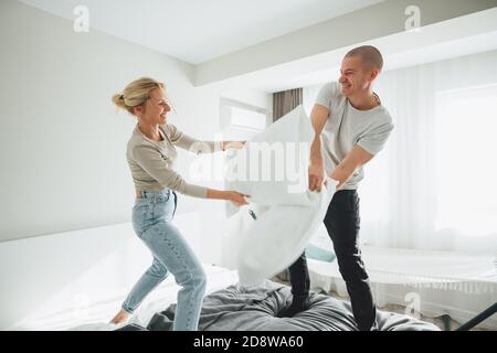 Una giovane coppia combatte sui cuscini dell'appartamento. L'uomo e la donna felici si ingannano intorno mentre sedendo a casa Foto Stock
