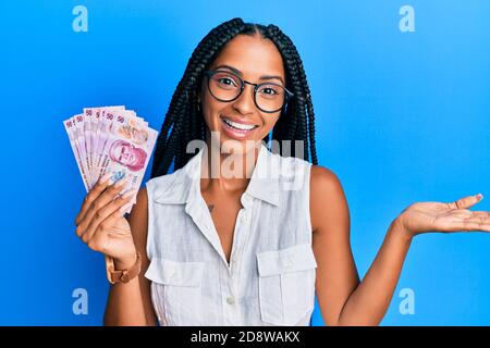 Bella donna ispanica in possesso di 50 pesos messicani banconote celebrare il successo con sorriso felice e espressione vincente con mano sollevata Foto Stock