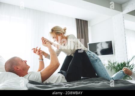 I giovani giocano e si divertono mentre si siedono a casa. La coppia felice si trova a letto e si stolge intorno a. Foto Stock