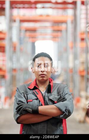 Giovane lavoratore misto-razza di magazzino in bracci di attraversamento uniforme grigio dal petto Foto Stock