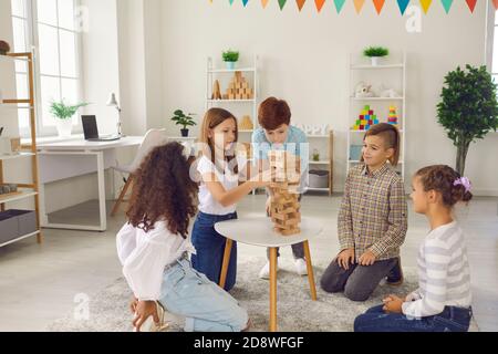 Gruppo di bambini sorridenti di razza mista seduti sul pavimento e. giocare con costruire piramide Foto Stock