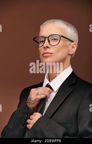 Elegante donna manlida con giacca nera, camicia bianca e cravatta da contatto per occhiali Foto Stock