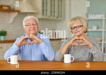 Sorridente coppia amorosa matura seduta e mostrando i cuori con le dita Foto Stock