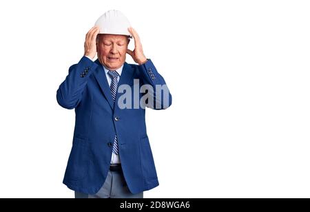 Uomo anziano bello grigio-capelli che indossa vestito e architetto hardhat che soffre di mal di testa disperato e stressato perché dolore e emicrania. Mani su Foto Stock