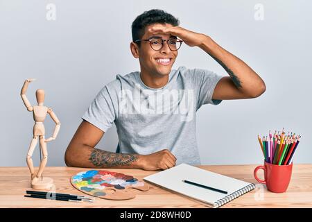 Giovane bel pittore afroamericano uomo seduta tavolozza e manichino d'arte molto felice e sorridente guardando lontano con mano sulla testa. Ricerca con Foto Stock