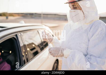 Medico che esegue un test PCR COVID-19 su un paziente attraverso la finestra dell'auto. PCR diagnostica per la presenza di Coronavirus, medico in kit di prova DPI Foto Stock