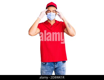 Giovane bell'uomo ispanico che indossa uniforme di consegna e maschera medica che soffrono di mal di testa disperata e stressata perché dolore ed emicrania. Mani Foto Stock