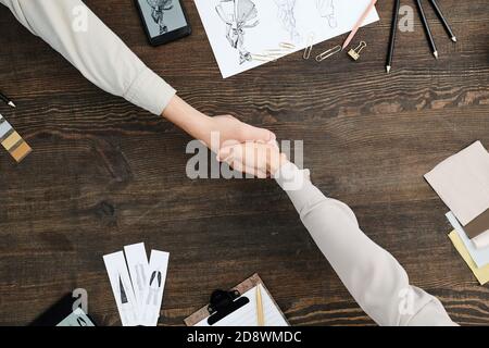 Panoramica della stretta di mano di due giovani stilisti contemporanei oltre tabella Foto Stock
