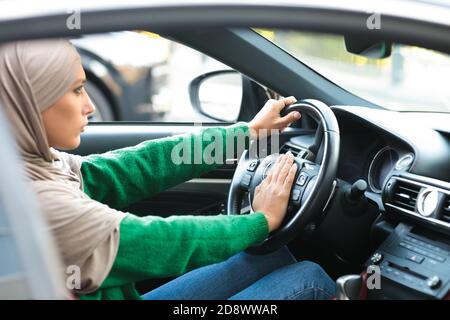 Donna musulmana seria che guida la sua auto e honking Foto Stock