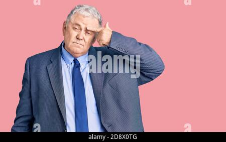 Uomo senior con capelli grigi che indossa giacca da lavoro puntando infelice a pimple sulla fronte, brutta infezione di blackhead. Acne e problema di pelle Foto Stock