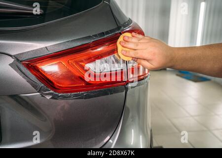 Mano di lavoro lucida il faro con spugna e pasta lucidante cera, il ripristino dei fari in Auto Detailing Service. Foto Stock