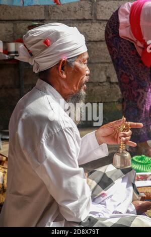 Primo piano di una pedanda indù durante la preghiera. Vista laterale di un sacerdote seduto. Il sacerdote tiene in mano una campana ed esegue la cerimonia. Benedizione di nozze Foto Stock