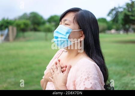 Donna asiatica in maschera e si sente malsano messo mano dove è polmoni, che soffre di tosse ripetuta e difficoltà alito. Foto Stock