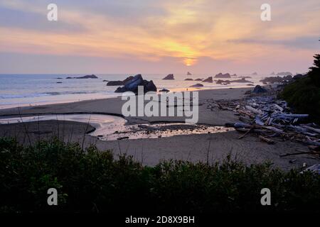 Le pile di mare, gli affioramenti rocciosi e il torrente che scorre nel mare, formano uno splendido sfondo per il tramonto sull'Oceano Pacifico. Area ricreativa statale di Harris Beach Foto Stock