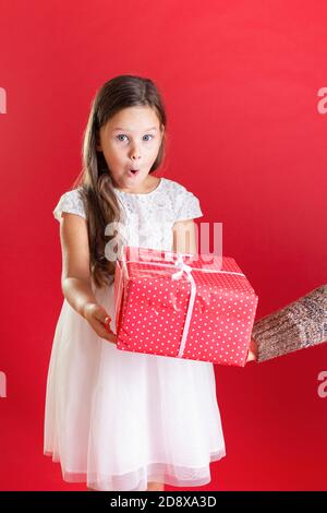 primo piano una ragazza in bianco è sorpreso di accettare una scatola regalo rossa da un'altra persona su un isolato sfondo Foto Stock