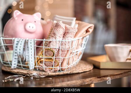 Attrezzi da cucire di forbici da sartoria, metro a nastro, tessuto di pizzo rosa in canestro a rete e rocchetti di filo e banco di pig. Foto Stock