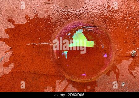 La vista dall'alto di una mezza bolla di sapone si trova su un mattone rosso incrinato. Acqua saponata con riflessi colorati Foto Stock