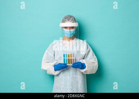 Concetto di covid-19, pandemia e salute. Immagine di un medico tecnico di laboratorio femminile, indossando dispositivi di protezione individuale, contenente provette con vaccino Foto Stock